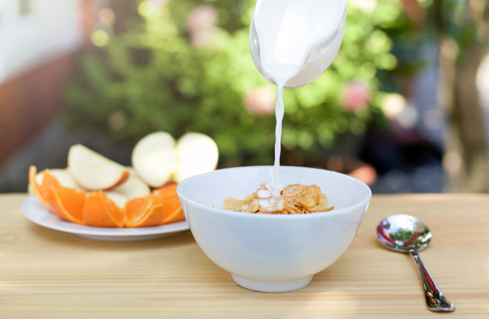 pouring-milk-into-bowl-corn-flakes-plate-fresh-fruit